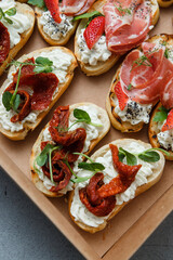 
A set of different snacks for a party or a festive table. Ciabatta sandwiches with tomatoes, jamon, cream cheese, vegetables, chambers and olives. Delicious wine snacks
