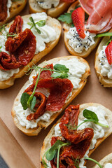 
A set of different snacks for a party or a festive table. Ciabatta sandwiches with tomatoes, jamon, cream cheese, vegetables, chambers and olives. Delicious wine snacks