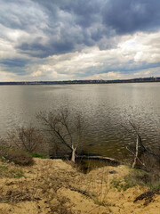 Morning nature landscape: river with blue dark clouds and branches on the other bank, spring, with sun rays on the water