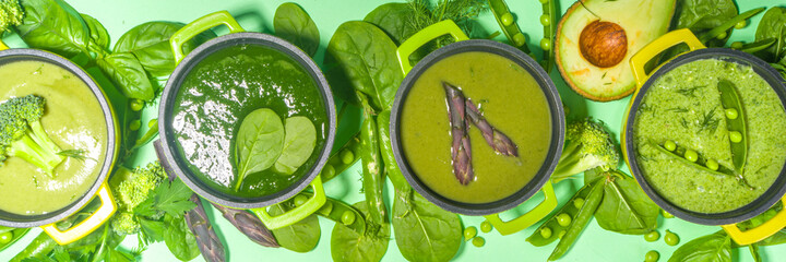 Green cream-soup set. Variety of classic green vegetable soups, in small portioned pots - asparagus, spinach, broccoli, green peas . over green background copy space top view