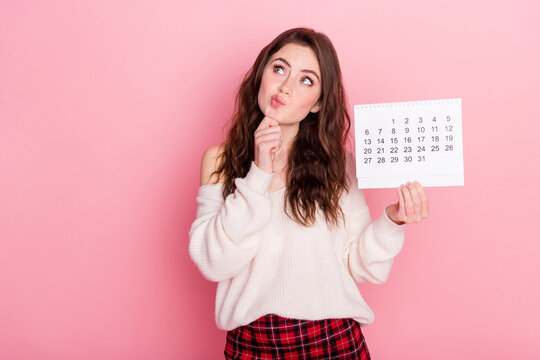 Photo of unsure thoughtful woman dressed white sweater arm chin holding calendar empty space isolated pink color background