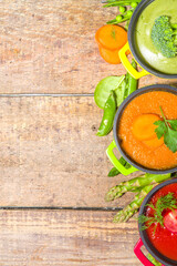 Set of various colored vegetable soups.Variety of classic vegetable cream soups, in small portioned pots - asparagus, spinach, broccoli, green peas, tomato, carrot. Wooden background copy space top vi