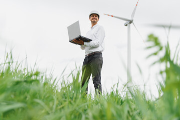 Engineering man using laptop to checking wind turbine generator of electricity at outdoor, blue sky...