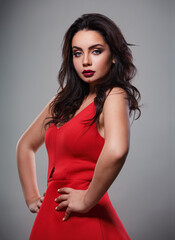 Fototapeta premium Beautiful makeup woman in red dress with long black curly volume hair style, burgundy lipstick with vamp look on grey background. Closeup