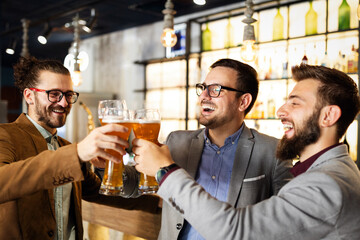 Happy young businessmen drinking beer and talking at pub after work