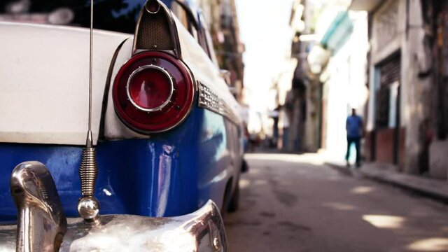Cinematic reveal from behind a 1950s classic car of a typical street in Havana Cuba