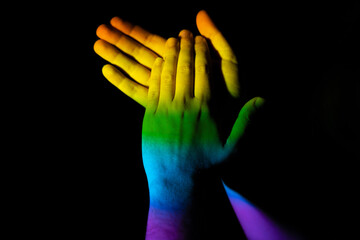 Clapping hands illuminated with the LGBT pride flag on a black background - victory concept