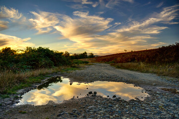 Summer sunset with clouds reflecting in puddle.