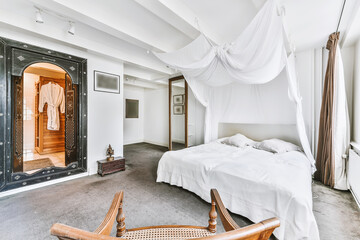 Interior of light bedroom with carpet flooring and white canopy above big bed in soft daylight