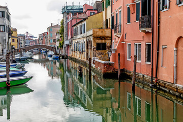 Fototapeta na wymiar Colorful houses of the ancient city of Chioggia, Venice lagoon, reflected in the water with boats and stone bridges 