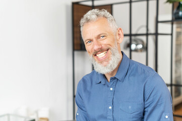 Fototapeta premium Portrait of charismatic senior middle aged man in smart casual shirt, handsome mature bearded businessman ceo looks at the camera with toothy smile