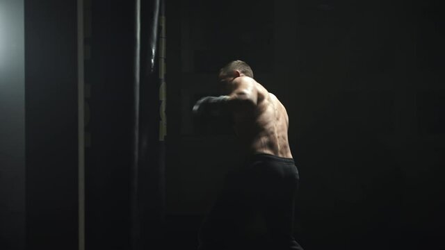 Kickboxer punching and kicking a boxing bag during a training,dark gym.