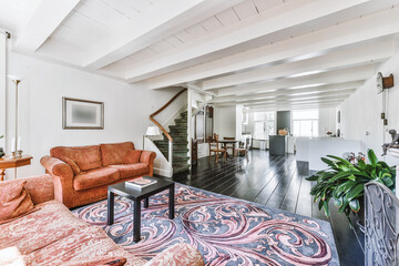 House sun lit room with terracotta sofas and ornamental carpet on wooden floor near staircase...