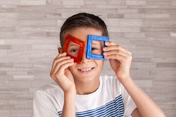 Child plays with a magnetic constructor. Boy playing with colorful toy blocks. Boy put the details of the constructor to the face like glasses.