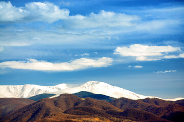 Snow covered mountain peaks with a beautiful blue sky and white clouds.