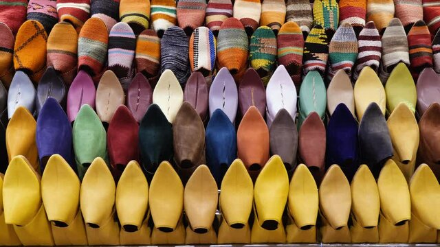 Authentic colorful Moroccan slippers (babouches), displayed on a wall, in the medina of Marrakech (Marrakesh), Morocco. Camera movement from left to right. Yellow babouches made in Fes (Fez).