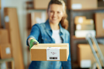 Smiling female in jeans in warehouse giving parcel