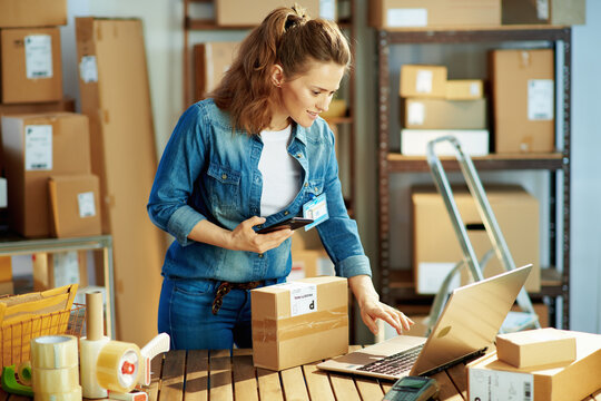 happy female in jeans using phone applications in warehouse