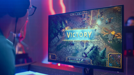Professional eSports Gamer Wins in RPG MOBA Mock-up Video Game on His Personal Computer. He is Using Headset. Cyber Gaming Stylish Retro Neon Room