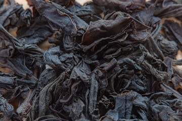 Dried tea pieces on a light surface. Black tea ready to brew, blurred in soft focus at high magnification.