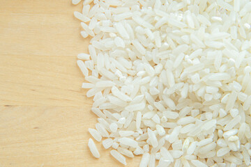 Raw rice grains on a wooden surface. Light background blurry in soft focus at high magnification.