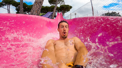 Selfie of a caucasian 40s man speeding down super fast sliding in a pink water slide at summer...