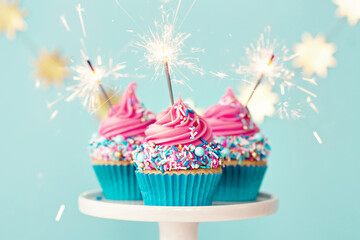 Three celebration cupcakes with pink frosting and sparklers