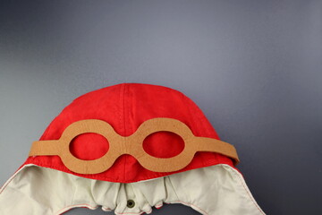 Children's red pilot hat with goggles on a gray background.