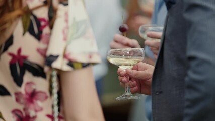 Man in suit stands and holds cocktail glass with champagne in his hands. Close-up of banquet, woman in elegant dress is standing nearby