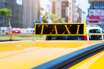 Word TAXI on roof of yellow cab at city street in summer day.