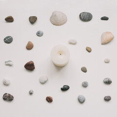 White candle and seashells and stones on white background. Spa concept. Flat lay, top view