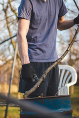 Detail of the deployment of a young temporary worker in a forest environment while cutting branches. Sharp scissors cut through a small tree stem like paper. The working season has begun