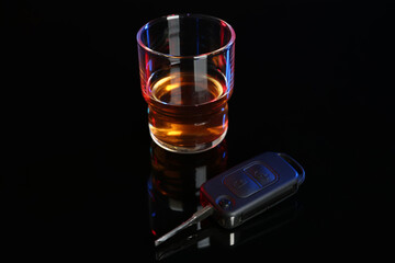 Car key near glass of alcohol on black table. Dangerous drinking and driving