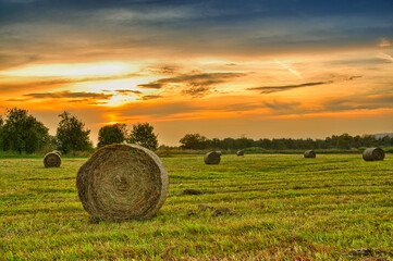 Golden sunset over farm field with hay bales