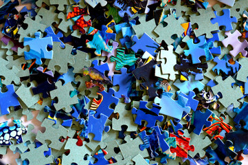 Close-up of a pile of unfinished white puzzle pieces. Many multicolored mosaic elements