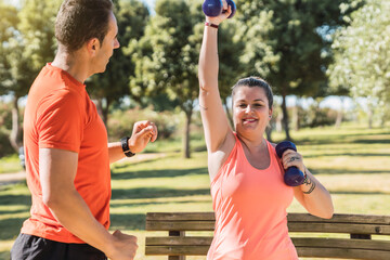 Obraz premium Woman in sportswear doing weights with a personal trainer