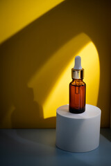Glass cosmetic bottle with oil or serum for skin care on special podium on yellow background. Shadows Natural skin care concept. Harsh shadows