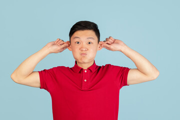 Half-length portrait of Asian young man isolated on blue studio background. Concept of human emotions