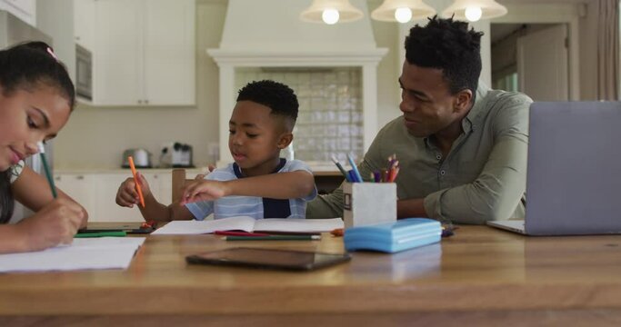 African american father, daugher and son sitting at kitchen table doing homework