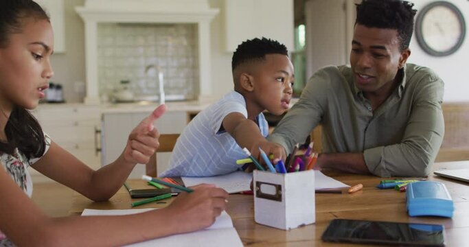 African american father, daugher and son sitting at kitchen table doing homework