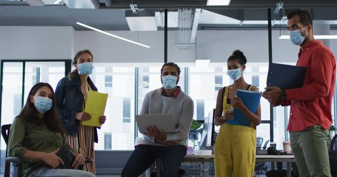 Portrait of diverse group of work colleagues wearing face mask holding laptop, tablet and documents