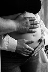Parents' hands lie on the belly of the pregnant woman. Young parents expecting a baby
