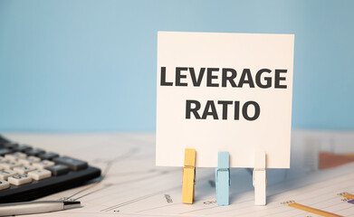 concept LEVERAGE RATIO on cubes against blue background near calculator and financial reports.