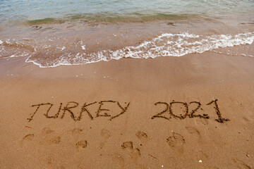 Fototapeta premium Turkey 2021. The inscription on the sand of the Turkish beach next to the waves of the sea. Holidays in Turkey in 2021.