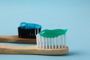 Wooden brushes with toothpaste on light blue background, closeup