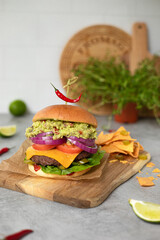 Burger Mexican style with guacamole lime red chilli hot pepper cheddar and nachos serve on wooden board with grey background
