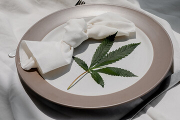 Cannabis friendly dinner concept. Beautiful dinner setup with marijuana leaf, knife and fork. Pastel colours. Copy space. 