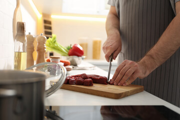 Man cutting meat to make bouillon in kitchen, closeup. Homemade recipe