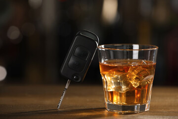 Car key and glass of alcoholic drink on wooden table against blurred background, space for text. Drunk driving concept
