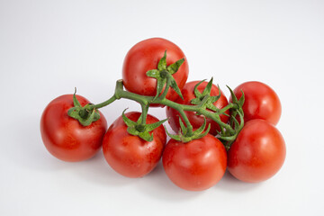 Red round tomatoes on a twig on a white background. Tomatoes branch with green leaves.